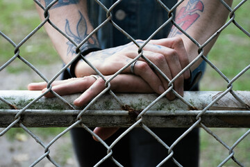 Tattooed hands of a young man seen through a football net in nature