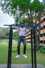 Young tattooed man doing pull-ups and parallel bars exercise in a public park surrounded by nature