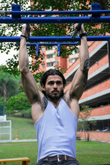 Young tattooed man doing pull-ups and parallel bars exercise in a public park surrounded by nature