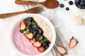 Presented by fruits putting yogurt toppings with strawberry, berry, oats, raisins and chia seed decorated by peppermint in white blow. Pink background. Set of healthy dairy product choice. Pecuniary.