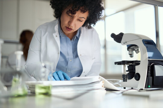 Female chemist doing some research while reading scientific books in laboratory - Powered by Adobe