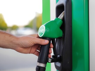Hand Holding Green HVO Fuel Pump Nozzle, Dropping Renewable Fuel at Eco-Friendly Fuel Station, Clean Energy Concept
