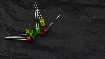 collection of red, green, and yellow LED diodes arranged on a dark crinkled paper surface, highlighting the different colors and detailed structure of the electronic components