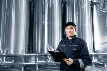 Female worker in modern beer factory with stainless steel tanks