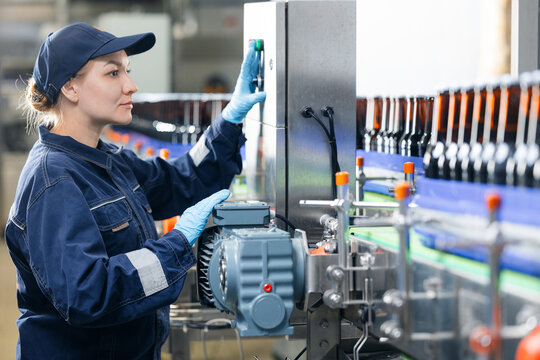 Female worker working on beer factory production line operating machinery, food industry