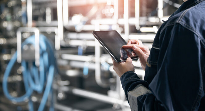 Concept food industry banner. Factory worker inspecting production line tanker in of dairy factory with computer tablet