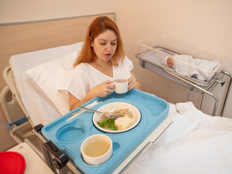 Caucasian woman eats on hospital bed after giving birth.  - Powered by Adobe