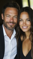 A man and woman are smiling for the camera. The man is wearing a suit and the woman is wearing a black dress. They appear to be happy and enjoying each other's company