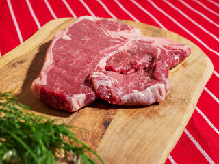 Fresh uncooked T bone steak with fresh dill and garlic cloves on wooden cutting board and on classic red and white stripe table cloth. High quality beef meat product. Butcher craft.