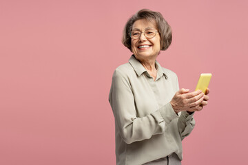 Happy senior woman using smartphone looking away smiling on pink background