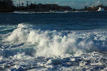 Big waves on the rocky picturesque seashore in Malta. Waves with spray crash onto the shore on a beautiful day with the setting sun.