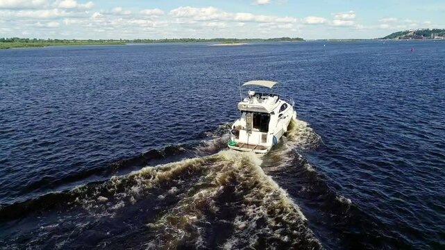 Boat is on the water with a blue sky in the background. The boat is moving and creating ripples in the water. Summer river trips along the Volga River in Nizhny Novgorod, Strelka.