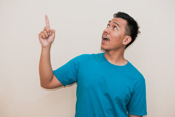 A Southeast Asian man in a turquoise green tshirt smiling and finger pointing to up right a white...