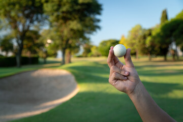 Hand Holding biodegradable Golf Ball on Green Golf Course Near Sand Bunker.