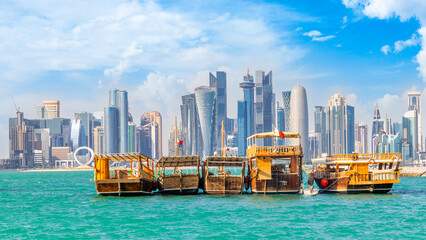 Traditional arab dhow fishermen boats with qatari flag at the sea bay with Doha futuristic business downtown center skyline, Qatar