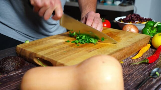 Chef hands in home kitchen cutting up fresh flat parsley on a wooden cutting board. Preparation of vegetables for cooking. Vegetarian cooking.