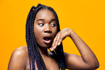 Surprised young woman with braids against a vibrant yellow background, expressing excitement and...