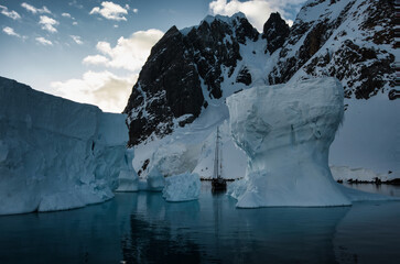 Antarctic Peninsula: Snowy peaks, icebergs, cloudy sky. Lemaire Channel