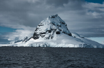 Antarctic Peninsula: Snowy peaks, icebergs, cloudy sky. Lemaire Channel