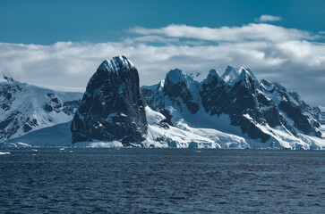 Antarctic Peninsula: Snowy peaks, icebergs, cloudy sky. Lemaire Channel