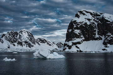Antarctic Peninsula: Snowy peaks, icebergs, cloudy sky. Lemaire Channel