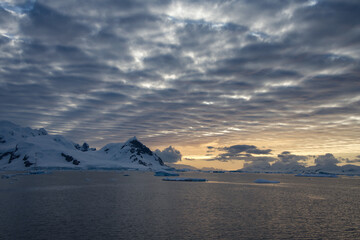 Antarctic Peninsula: Snowy peaks, icebergs, cloudy sky. Lemaire Channel