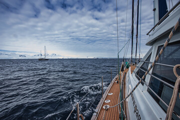 Antarctic Peninsula, A sailboat navigates choppy waters near snowy Antarctic mountains.