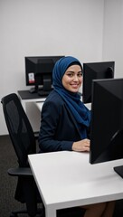 Young Muslim Woman in Professional Attire Working at a Modern Office Desk with Computers in a Bright, Minimalist Workspace