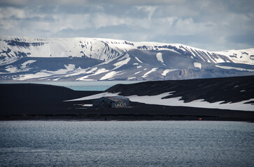 Deception Island, Antarctica:  Rusty building, snow-capped hills, blue water.