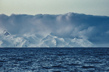 Antarctic Peninsula, Drake Passage:  Snowy mountains, calm sea.