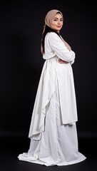 Naklejka premium Elegant Young Arab Woman in Traditional White Dress and Hijab Posing Confidently Against a Dark Background, Showcasing Cultural Heritage and Modern Fashion Aesthetic