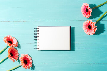 Blank spiral notebook with pink gerbera flowers on a turquoise wooden background with sharp...