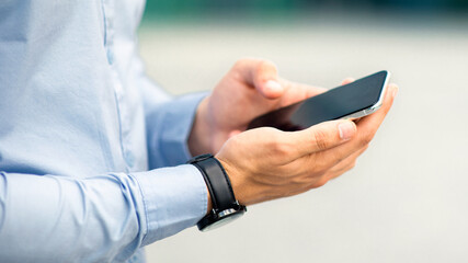 Unrecognizable businessman standing by office center, holding modern smartphone with blank screen, checking business process online, using mobile business application, closeup, copy space