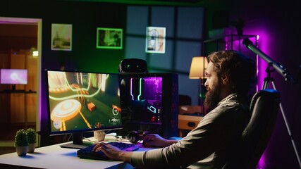 Man in dark living room playing science fiction videogame on gaming PC, relaxing by shooting...