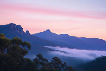Rugged mountain range bathed in soft pink hues with mist curling through the valley