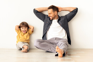 Relax time. Happy little boy sitting with daddy and laughing to camera, sitting together on floor...