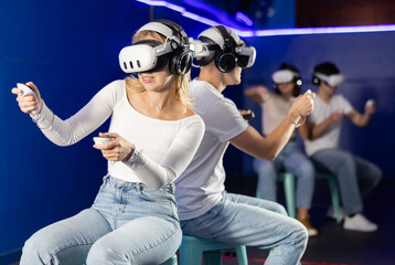Friends play against each other in pairs in virtual reality helmets and with joysticks in their...