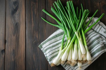 A bunch of fresh scallions on a striped kitchen towel, set against a dark wooden background. Vibrant greens and whites.