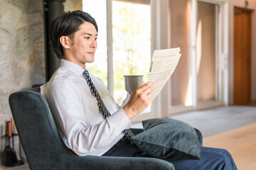 朝家で英字新聞を読むスーツ姿のアジア人ビジネスマン
