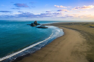 Tranquil Whatipu beach scene. Lone person walks along the shore, waves crash on the dark sand....