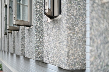A textured terrazzo-framed window set on a clean white brick wall, highlighting a blend of Japanese and modern minimalist design. The uniform row of glass windows enhances the structural harmony.