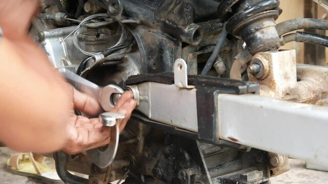 A mechanic's hand opens a motorcycle shockbreaker bolt for maintenance, repair and service