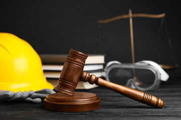 Accident at work concept. Gavel, books, scales and construction worker's protective gear on black...