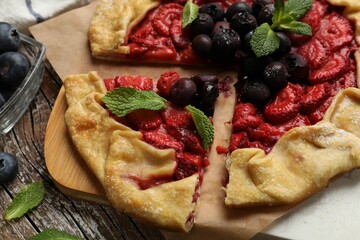 Tasty galette with strawberries, blueberries and mint on wooden table, closeup