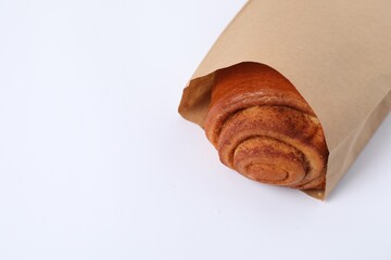 Paper bag with freshly baked bun on white background, closeup. Space for text