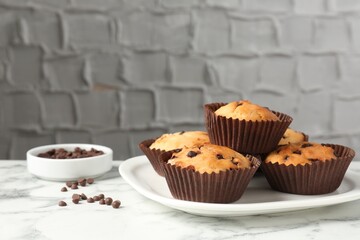 Delicious muffin with chocolate chips on white marble table, closeup