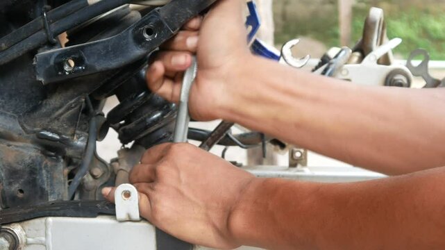 A mechanic's hand opens a motorcycle shockbreaker bolt for maintenance, repair and service