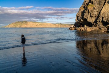 A young girl walks along the beach, while fishermen cast lines from the rocks. Coastal scene at...
