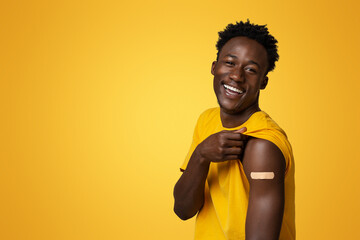 Cheerful Black Guy Showing Arm With Plaster After Successful Covid-19 Vaccination Shot, Portrait Of Happy Young African American Man Got Vaccinated Against Coronavirus, Beige Background, Copy Space