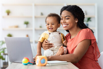Happy Young Mom Working On Laptop And Taking Care About Baby At Home, Smiling African Lady Holding...